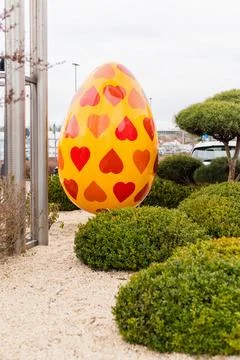 A big yellow Easter egg covered in red heart shapes is placed in a green ga.. Stock Photos