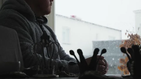 Bigger man sitting in the kitchen drinking coffee while it is snowing outside Stock Footage 150215205