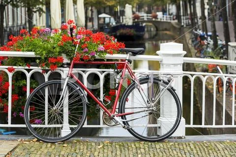 Bike along white metal railing on stone bridge with colourful flowers in box and Stock Photos