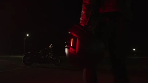 Biker in black leather jacket goes with a helmet in his hand to his motorcycle Vidéo 292775422