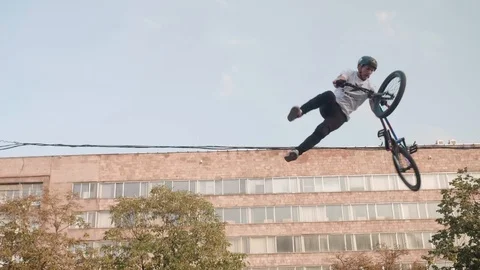 Biker hops off and does trick on his BMX bicycle. Old building on background. Stock Footage 120731882