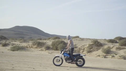Biker performing stunts while riding his motorcycle on desert road Stock Footage 85826313