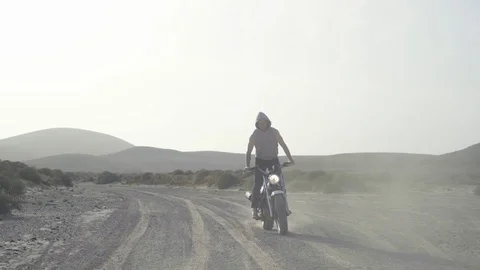 Biker performing stunts while riding his motorcycle on desert road Stock Footage 85826366