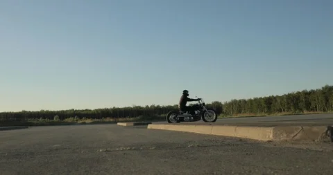 Biker quickly rides a motorcycle on the road near the forest at sunset, side Stock Footage 111997832