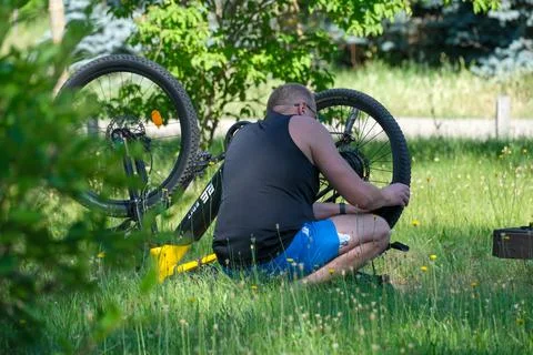 Biker repairs flat tire in sunny green park on a warm afternoon Stock Photos