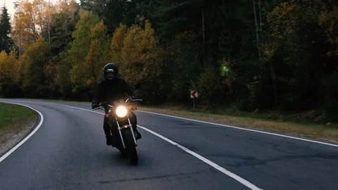 Biker rides a vintage retro motorcycle along a scenic forest road in autumn. Stock Footage