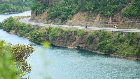 Biker riding on road besides river Видео 88676531