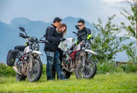 Bikers checking map next to off road motorcycles, mountains in background, Stock Photos