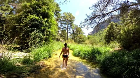 Bikini girl walking down the stream of a river through the forest Stockbeeldmateriaal 135089955