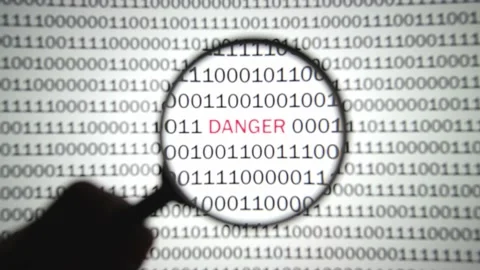 Binary code with a red label danger is viewed with a magnifying glass. 스톡 동영상 144633558