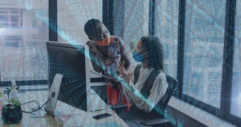 Binary coding over two diverse female colleagues wearing face masks discussing Stock Footage 327642384