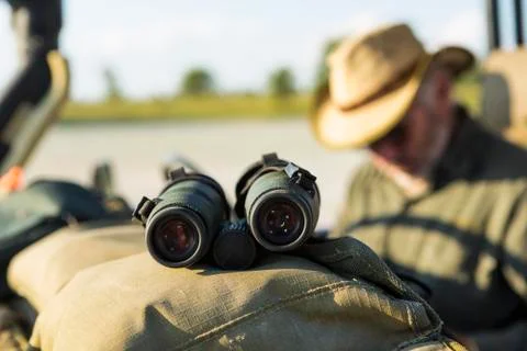 Binoculars on the dash of a safari jeep, a safari guide in the background. Stock Photos