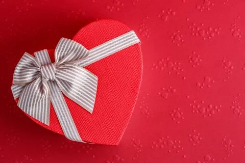 Biodegradable cardboard gift box in the shape of a heart with ribbons on red  Stock Photos