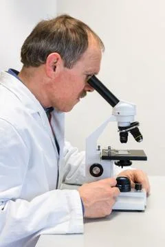 Biologist in lab coat looking through microscope Stock Photos