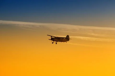 Biplane flying alone in vibrant orange sunset Stock Photos
