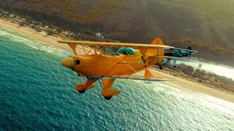 Biplane flying over a beautiful ocean coastline at sunset in a dynamic aerial Stock Footage 343695779