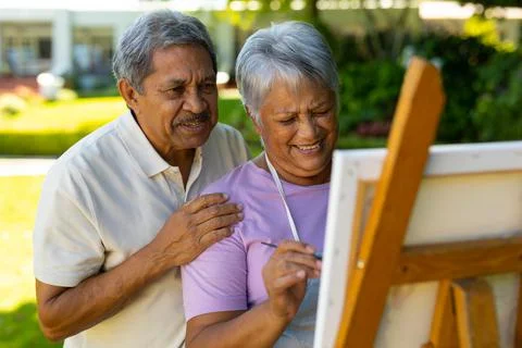 Biracial senior husband standing with smiling senior wife painting on canvas in Stock Photos
