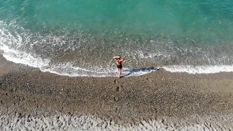 Bird eye view man goes on rocky beach into water and swims Video stock 103182947