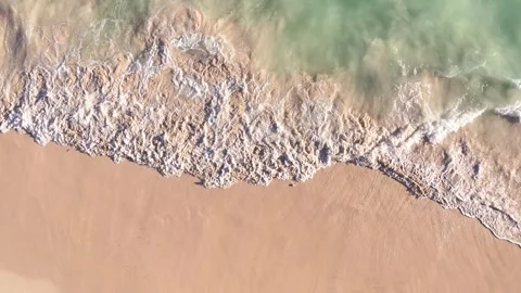 Bird-eye view of ocean waves down below crashing onto the sandy shore in Summer. Stock Footage 300503249