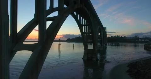 Bird flies underneath the bridge at sunset (aerial) (Newport, OR) Stock Footage 67647440