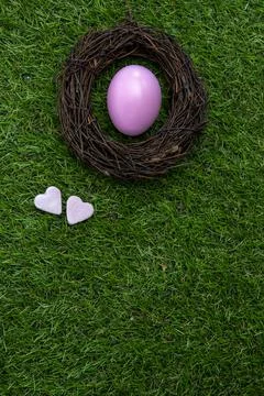 Bird nest with a Easter egg on green grass and two pink candy hearts. Stock Photos