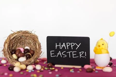 Bird nest full of easter almond eggs, decorative chick and blackboard Stock Photos