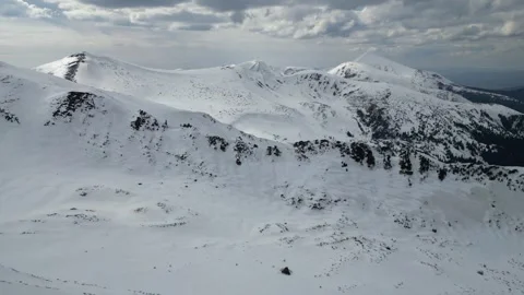 A bird view of a snowy rocky mountain range with a cloudy sky in the backgr.. Stock Footage 240629009