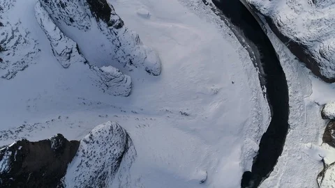 Birds eye looking down and flying over a river in a snow covered canyon/valley. Video stock 88227169