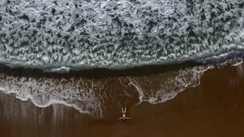A bird's-eye view of a man lying on a sandy empty beach. Sandy beach and waves Stock Footage 230381453