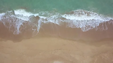 Bird's eye view of ocean waves crashing against an empty beach from above, Stock Footage 153279728