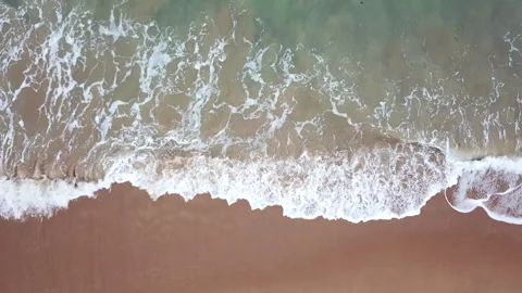 Bird's eye view of ocean waves crashing against an empty beach from above, Stock Footage 153281106