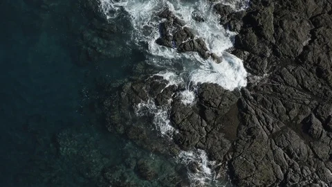 Bird's eye view pull back of ocean waves crashing onto a rock shoreline Stock Footage 103344052