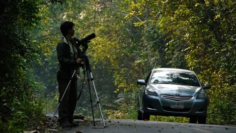 Birdwatcher with scope and binoculars on road with cars passing by. Stock Footage 121617953