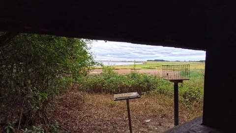 Birdwatching hide looking out onto waterfront estuary marshland pull back Stock Footage 342342097