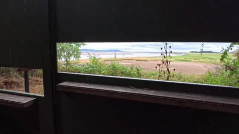 Birdwatching hide looking out onto waterfront estuary marshland pan left Stock Footage 342342131