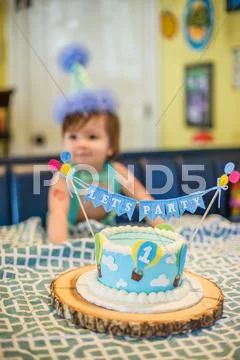 Birthday Cake In Front Of Baby Boy Wearing Party Hat At Table