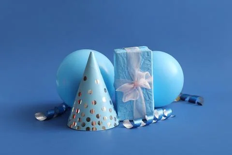 Birthday composition with party hat, gift box and balloons on blue background Stock Photos