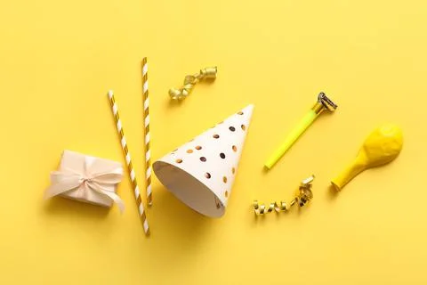 Birthday composition with party  hat, gift box and whistle on yellow backgrou Stock Photos