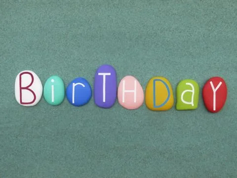 Birthday text composed with multicolored stone letters over green sand Stock Photos