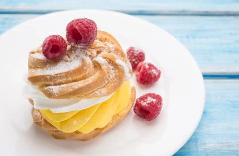 Biscuit cake with raspberry berries on a white plate. On blue wooden table. Stock Photos