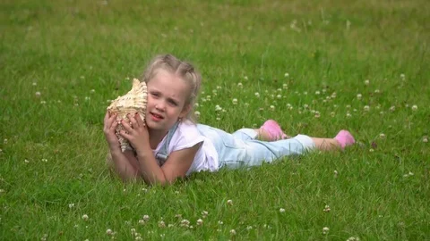 A bit the fair-haired girl listens to a surf of waves in a big cockleshell. The Stock Footage 77470232