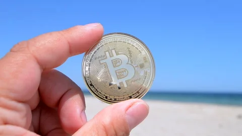 Bitcoin BTC coin close-up. Man holding bitcoin coin hand on background blue sky Stock Footage 246090506