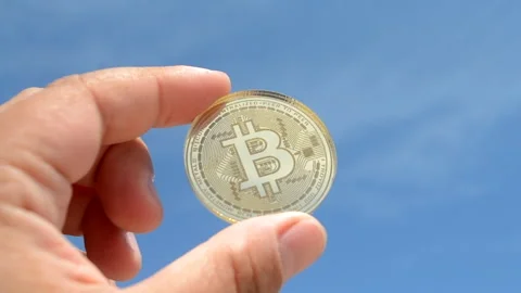 Bitcoin BTC coin close-up. Man holding bitcoin coin hand on background blue sky Stock Footage 247376174