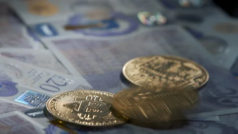Bitcoin BTC coin rotating on bills of 20 pounds. Coins falling on Stock Footage 258835212