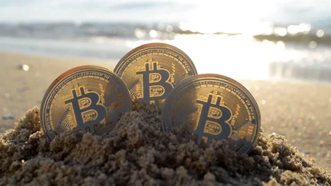 Bitcoin BTC coin in sand on sandy beach of sea coast on a sunny morning close-up 動画素材 296121694