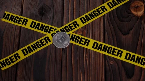 Bitcoin is a coin on a brown surface with a yellow ribbon with the word DANGER Stock Footage 329913672