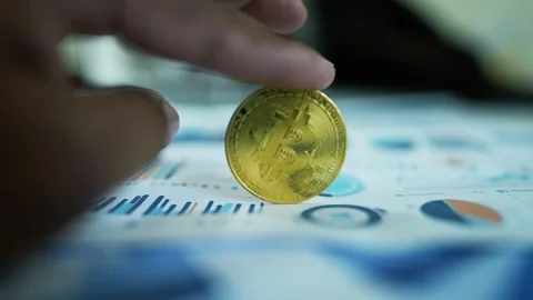 Bitcoin Coin Held Over Financial Charts, A hand holding a Bitcoin coin over.. Vídeos de archivo 304880554