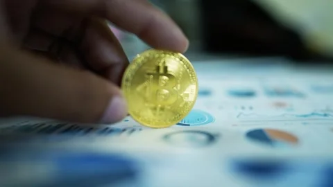 Bitcoin Coin Held Over Financial Charts, A hand holding a Bitcoin coin over.. Stockbeeldmateriaal 304880738