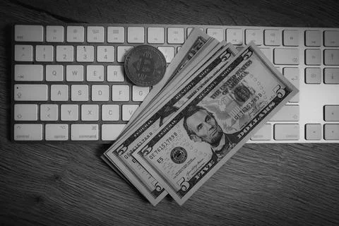 A Bitcoin coin lies on the desk next to a few dollar notes on a computer ke.. Stock Photos