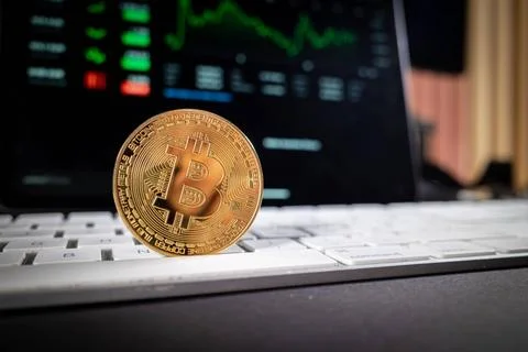A bitcoin coin is standing on a computer keyboard and in the background is... Stock Photos